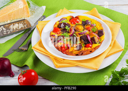 Cuite au four frittata savoureux avec l'aubergine, tomate et oignon rouge saupoudré de persil plat blanc de fromage parmesan et de légumes sur une table en bois, Banque D'Images