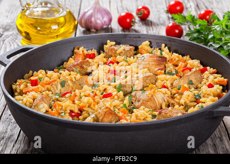 Paella maison préparé avec de la viande, le poivre, les légumes et les épices à la cocotte sur planches en bois, bouteille d'huile d'olive, tomates, persil, ail, sur Banque D'Images