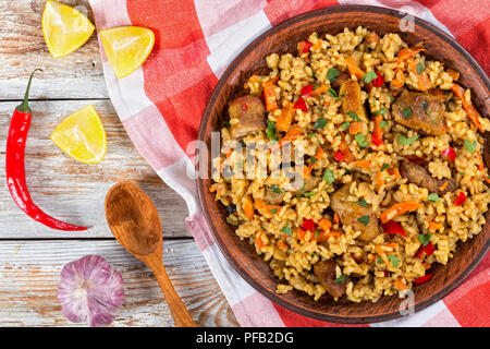 La paella avec de la viande, le poivre, les légumes et d'épices sur un plat d'argile, essuie-tout,tranche de citron, l'Ail, piment et cuillère en bois blanc sur l'écaillage de la peinture Banque D'Images