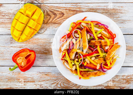 Crumbed pain de viande de poulet, mangue, les arachides, le poivron, l'oignon rouge sur blanc salade plat avec la moitié de la mangue en cubes et le poivron sur blanc p Banque D'Images