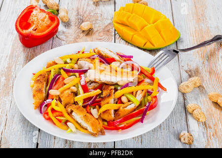 La mangue, crumbed pain, viande de poulet, les arachides, le poivron, l'oignon rouge sur blanc salade plat avec la moitié de la mangue en cubes, close-up Banque D'Images