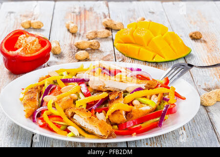 La mangue, crumbed pain, viande de poulet, les arachides, le poivron, l'oignon rouge sur blanc salade plat avec la moitié de la mangue en cubes, close-up Banque D'Images