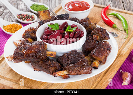 Côtes levées grillées coupées en chinois simple récipient blanc sur les côtes avec red bean dans bol, sur planche à découper, de la sauce tomate en saucière et épices sur ba Banque D'Images