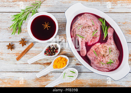 Cuisses de canard cru mariné dans la préparation pour la cuisson du vin avec le romarin et le zeste d'orange dans le plat à gratin, bol avec le vin rouge, l'anis étoilé, les épices dans Banque D'Images