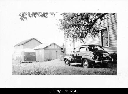 Photographie noir et blanc, montrant un trois-quart, vue partielle d'un profil brillant, noir, vintage Chevrolet Sedan, stationné à l'extérieur en face d'une maison en bois de banlieue, avec un hangar et caravane à l'arrière-plan, probablement photographié en Ohio dans la décennie suivant la Seconde Guerre mondiale, 1950. () Banque D'Images