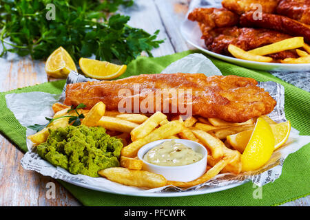 Croustillant de délicieux fish and chips - Cabillaud frit, frites, rondelles de citron, de sauce tartare et purée de petits pois sur la plaque sur le papier. le persil et quartiers de citron sur w Banque D'Images