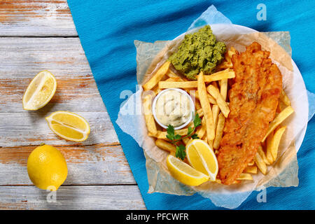 Croustillant de délicieux fish and chips - Cabillaud frit, frites, rondelles de citron, de sauce tartare et purée de petits pois sur la plaque sur le papier sur la vieille table en bois, authentique Banque D'Images