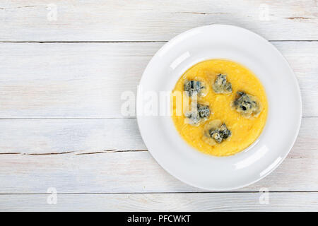 Polenta crémeuse délicieux chaud avec du fromage gorgonzola fondu sur plaque blanche sur la vieille table en bois blanc, recette authentique, vue de dessus, l'espace vierge fo Banque D'Images