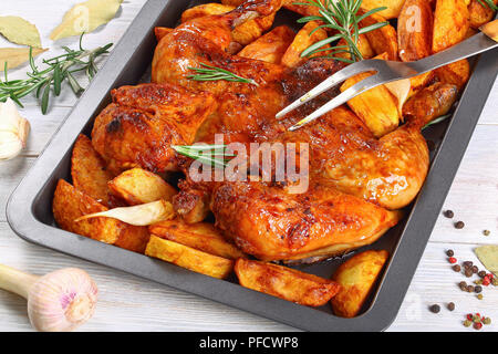 Poulet grillé croustillant d'or sur la plaque de cuisson avec les quartiers de pommes de terre, l'ail et le romarin.. fourchette à découper. Ingrédients sur fond blanc, vue à partir de Banque D'Images