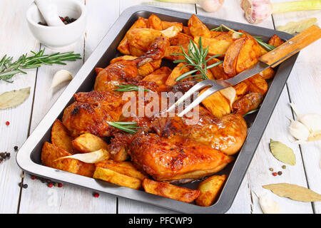 La peau du poulet grillé croustillant d'or sur la plaque de cuisson avec les pommes de terre, l'ail. romarin. et fourchette à découper. mélange de poivre, le laurier, l'ail et au romarin Banque D'Images