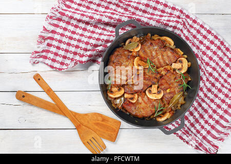 Délicieux filet de porc aux oignons ragoût de champignons., romarin, vin blanc demi-sec et d'épices en fer blanc ragoût casserole sur table avec des essuie-tout et du bois Banque D'Images