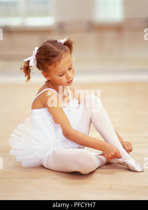 Danseuse de ballet Girl wearing white de danseur et tutu sitting, mettre sur les chaussures de ballet. Banque D'Images