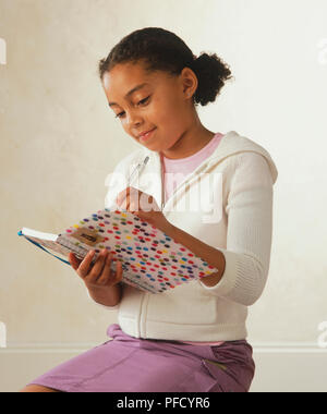 Girl écrit dans un bloc-notes avec un stylo. Banque D'Images
