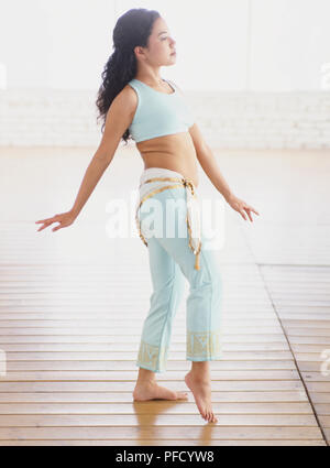 La femme en bleu soutien-gorge de sport et des jambières en faisant un pas en avant, genou légèrement plié et les orteils touchent le sol, les bras légèrement étendu sur le côté, vue de côté. Banque D'Images