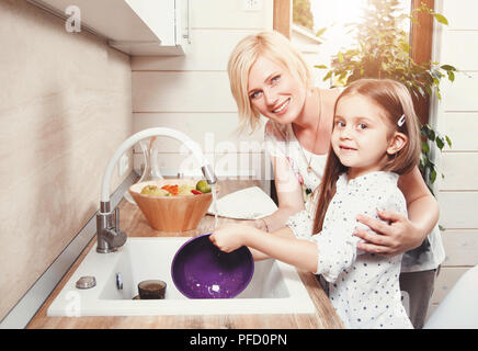 Belle blonde mère et fille cute brunette peu laver la vaisselle sur la cuisine légère, le soutien de la famille concept Banque D'Images