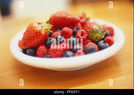 Bleuets, fraises et framboises rouges en blanc rond plat sur table en bois Banque D'Images