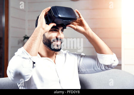 Bel homme arabe noir utilise des lunettes VR set assis sur le canapé en home studio Banque D'Images