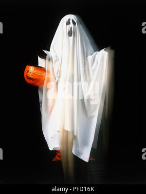 Personne portant couverture blanche avec ghost face peint sur tout en maintenant la lanterne citrouille, blurred motion. Banque D'Images