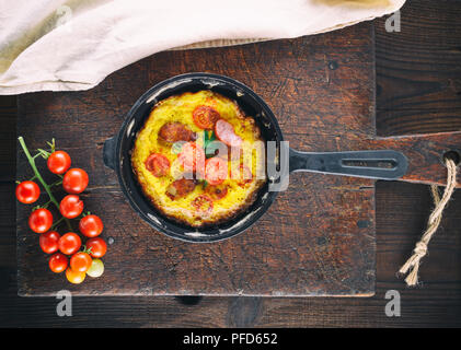 Poulet frit oeufs dans une ronde noire fonte poêle sur une vieille planche à découper en bois brun, vue du dessus Banque D'Images