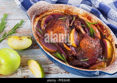 Cuisses de canard grillé au four cuit dans du vin rouge avec le romarin, le zeste d'orange et les tranches de pommes dans un plat à gratin, on table cloth, vert pomme sur peeling blanc pa Banque D'Images