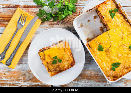 Partie de la moussaka délicieux sur plaque avec fourchette et couteau et dans plat à gratin sur de vieilles planches en bois, la cuisine traditionnelle grecque, recette authentique, vue Banque D'Images