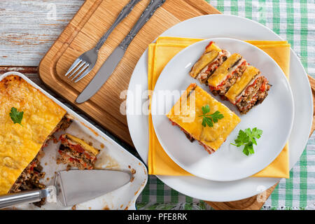 Partie de la moussaka en couches délicieux décoré de persil coupé en tranches cuites recette authentique, sur des plateaux avec serviette et dans plat à gratin, Banque D'Images