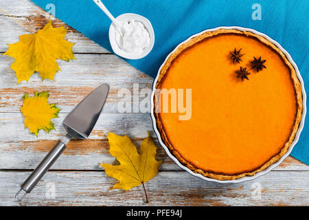 Délicieux faits maison orange vif pumpkin pie ouvert dans le plat de cuisson. de crème fouettée, de feuilles d'érable gâteau sec et pelle sur l'écaillage de la peinture blanche, table rustique Banque D'Images