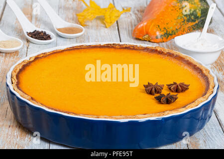 Ouvrir la citrouille orange vif délicieux gâteau dans le plat de cuisson. de crème fouettée, de feuilles d'érable et épices sèches sur l'écaillage de la peinture blanche table rustique, authentique loisir Banque D'Images