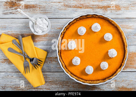 Ouvrir la citrouille orange vif délicieux gâteau dans le plat de cuisson décoré de crème fouettée, avec dessert fourchettes sur serviette et crème en saucière sur vieux tabl Banque D'Images