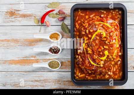 La viande de porc cru préparé pour rôtir au four, mariné à la sauce barbecue avec la moutarde, l'oignon, fines herbes et épices dans le plat de cuisson sur le background en bois Banque D'Images