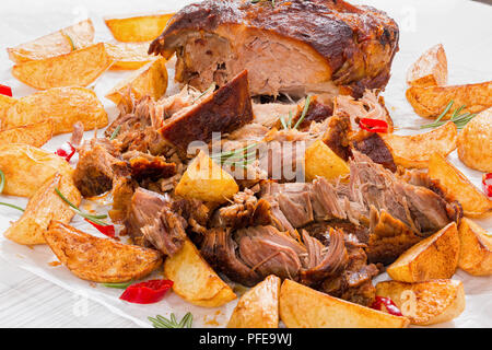 Quartiers de pommes de terre frites et gros morceau de Oven-Barbecued mijotés, épaule de porc en fonction de cuisson recette authentique, sur un papier parchemin avec ros Banque D'Images