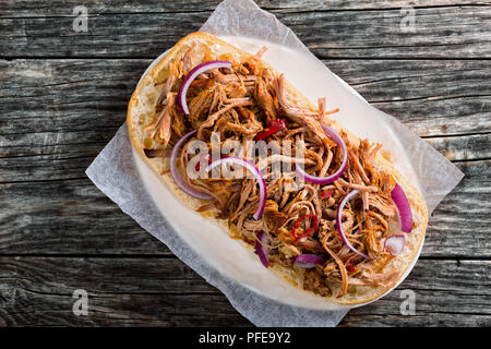 Porc barbecue ouvert avec Sandwich ciabatta, Sauce barbecue à l'oignon rouge et de piment sur le papier parchemin sur la plaque ovale sur la vieille table en bois sombre, vue Banque D'Images