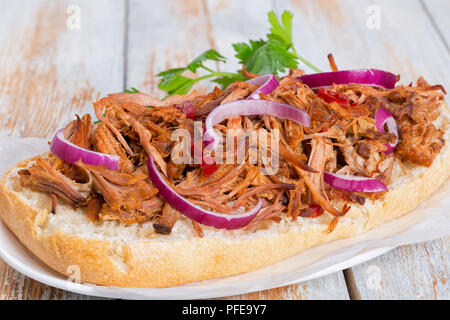 Porc barbecue ouvert avec Sandwich ciabatta, Sauce barbecue à l'oignon rouge et de piment sur le papier parchemin sur la plaque ovale sur de vieilles planches en bois blanc wit Banque D'Images