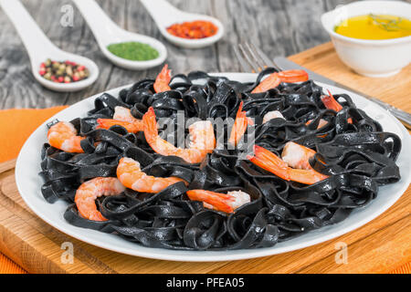 Delicious l'encre de seiche, crevettes nouilles avec noir sur blanc plat sur planche à découper avec de l'huile d'olive et des épices dans les cuillères sur background, close-up Banque D'Images