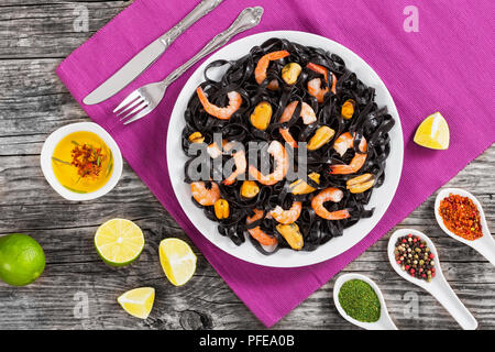 L'encre de seiche délicieuses nouilles noires avec les crevettes et les moules sur le plat blanc sur tapis de table sur une table en bois foncé avec de la chaux et des épices sur l'arrière-plan, vie Banque D'Images