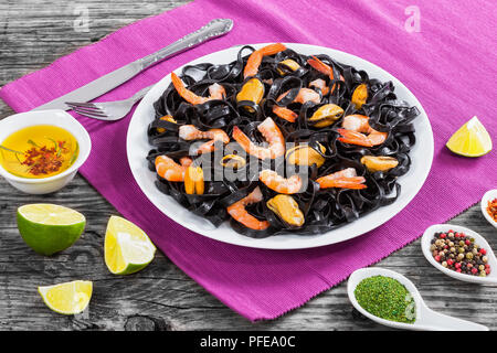L'encre de seiche délicieuses nouilles noires avec les crevettes et les moules sur le plat blanc sur tapis de table sur une table en bois foncé avec de la chaux et des épices sur l'arrière-plan, vie Banque D'Images