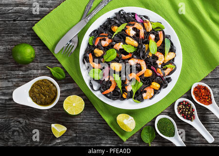 Délicieux avec la salade de nouilles noires crevettes, moules, frais vert épinards, laitue, roquette sur plat blanc sur tapis de table sur une table en bois foncé avec de la chaux sl Banque D'Images