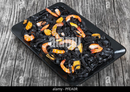 Salade de nouilles noires aux gambas et moules sur plateau rectangulaire noir sur table en bois foncé close-up, vue du dessus Banque D'Images