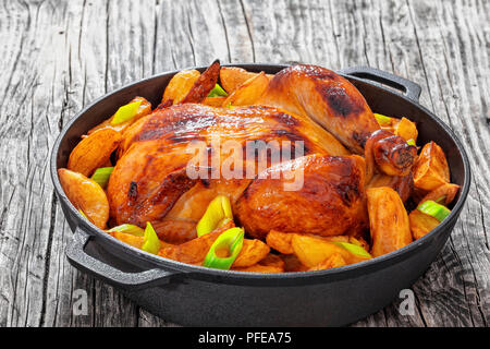 Poulet entier rôti frites avec les quartiers de pommes de terre et le poireau dans vieux poêle en fonte sur les planches de bois, close-up, vue d'en haut Banque D'Images