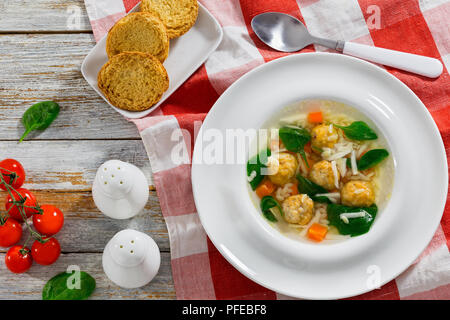 Soupe de noces italiennes avec des boulettes de viande dans la cuvette large blanc sur tapis de table, salière et poivrière, crostini, frais vert d'Épinards et tomates Banque D'Images