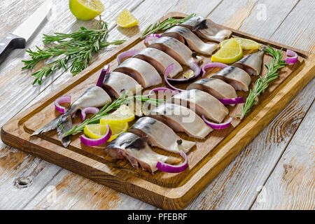 Filets marinés de maquereau poisson coupé en tranches sur la planche à découper avec le romarin, le citron, l'oignon rouge et d'épices, couteau et pièces citron o Banque D'Images