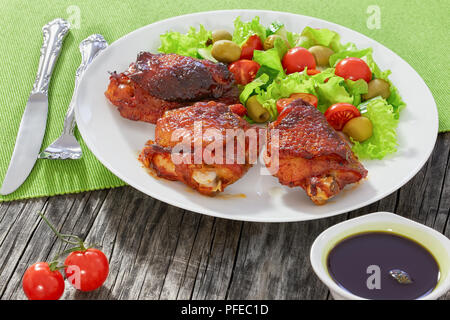 Cuisses de poulet grillées avec salade verte de laitue, concombre, tomates et olives sur plateau blanc, l'huile de graines de citrouille en vinaigrette saucière sur o Banque D'Images