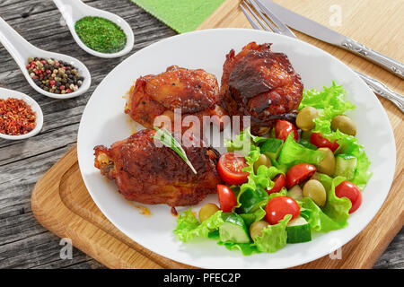 Cuisses de poulet rôti avec salade fraîche vert sur blanc plateau sur planche à hacher avec fourchette et couteau, graines de citrouille pansement en saucière sur vieux whit Banque D'Images