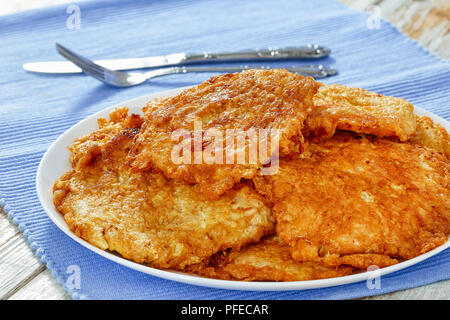 Oven-Fried côtelettes de porc sur le plat blanc tapis de table avec fourchette et couteau, sur fond de bois ancien, facile recette italienne, close-up Banque D'Images