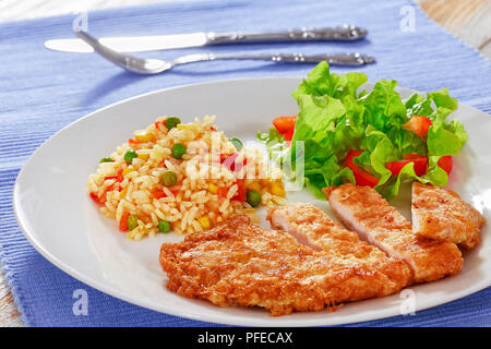 La viande dans la pâte frite délicieux chop avec risotto coloré et de la laitue fraîche salade de poivron sur plaque blanche sur le tapis de table, close-up Banque D'Images