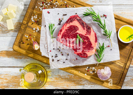 Faux-filet de boeuf de la viande fraîche le bifteck sur le livre blanc sur la planche à découper avec le romarin, ail, sel de mer casher, de beurre et d'huile d'olive sur l'ancien plan de travail en bois, Banque D'Images