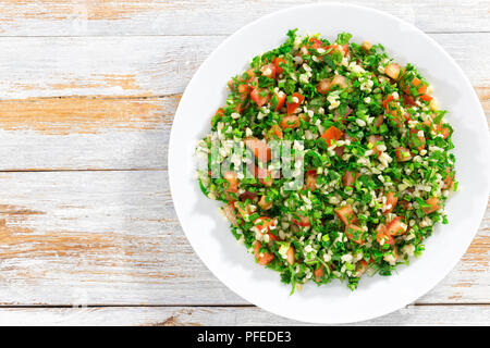 Salade de persil ou d'un taboulé sur plateau blanc, facile et sain plat végétarien classique de boulghour, tomates, persil, menthe et l'oignon de printemps sur sol en bois b Banque D'Images
