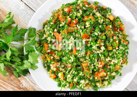 Boulgour végétarienne sans gluten,persil, menthe, oignon, salade de tomates arrosées de jus de citron et d'huile d'olive sur le plat blanc sur l'écaillage de la peinture t Banque D'Images