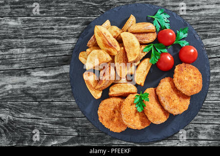 Close-up d'escalopes de poulet frit délicieux juteux sur ardoise plaque avec les quartiers de pommes de terre et les tomates sur la vieille table en bois rustique, vue de dessus, copyspac Banque D'Images