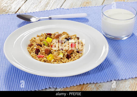 Petit-déjeuner sain - granola au miel, le gruau, la noix de cajou, pistaches, amandes, raisins et canneberges séchées en plaque blanche. verre de lait et une cuillère sur Banque D'Images